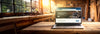 Laptop on a wooden table in a workshop setting, showcasing the Carbatec Shopify store launch with tools and woodworking equipment in the background.